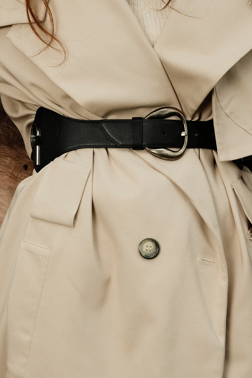 Close-up of a beige trench coat with a black belt and button detail.