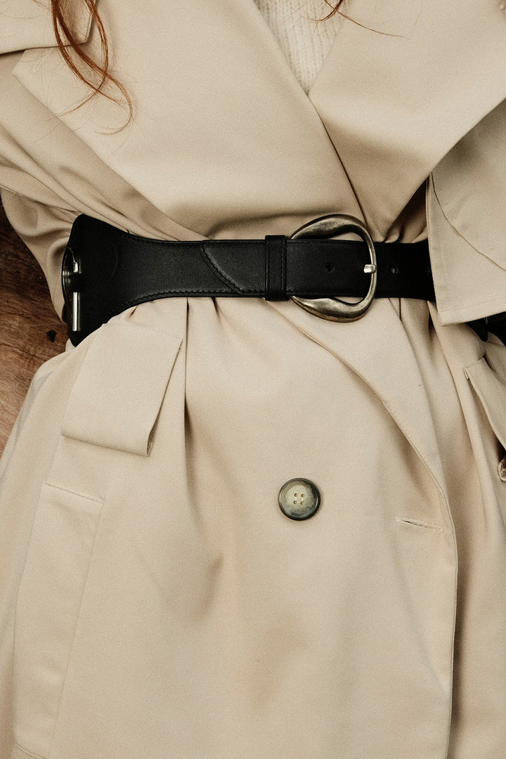 Close-up of a beige trench coat with a black belt and button detail.