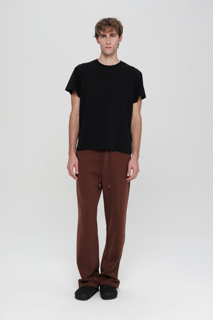 Person wearing a black t-shirt and brown pants on a white background