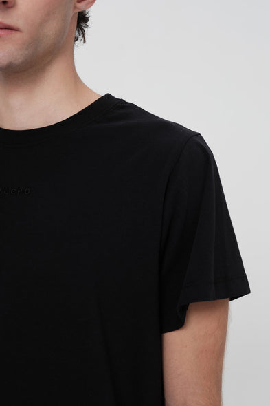 Person wearing a black t-shirt with a brand logo on a plain background