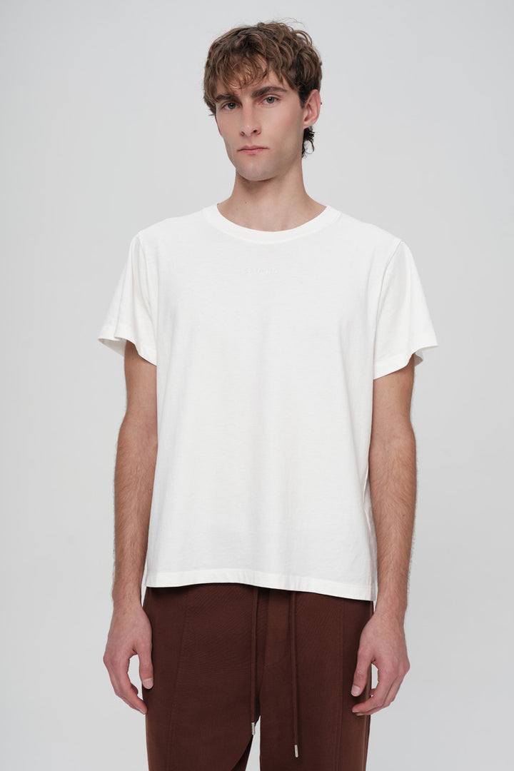 Man wearing a plain white t-shirt and brown pants on a light gray background