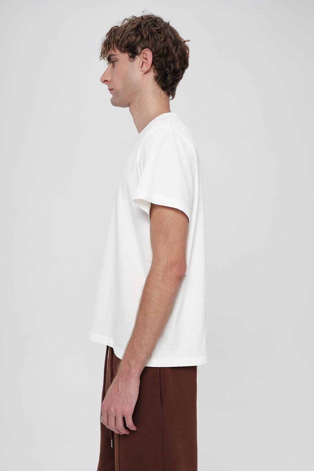 Person wearing a plain white t-shirt and brown pants on a light gray background