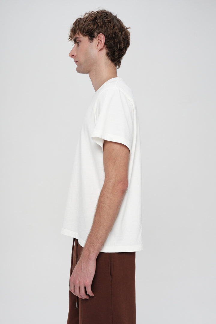 Person wearing a plain white t-shirt and brown pants on a light gray background