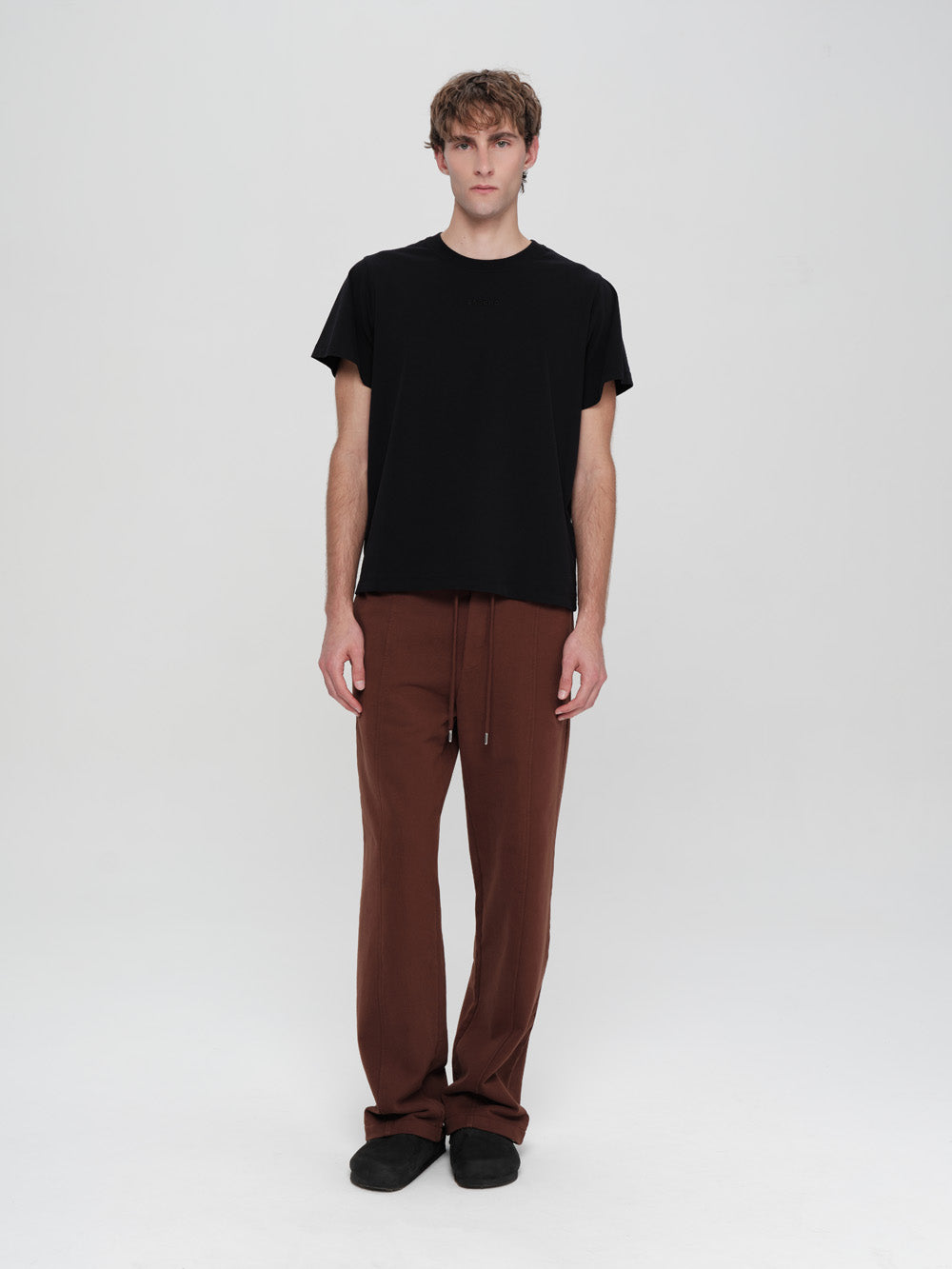 Person wearing a black t-shirt and brown pants on a white background