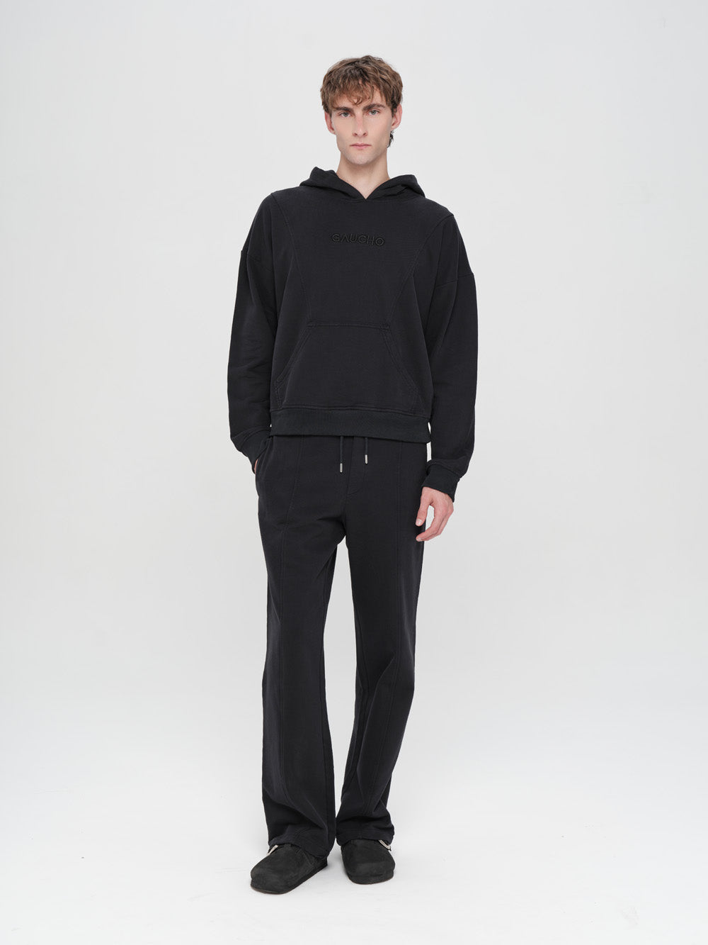 Person wearing a black hoodie and pants on a white background