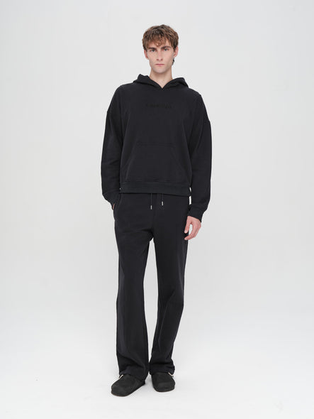 Person wearing a black hoodie and pants on a white background