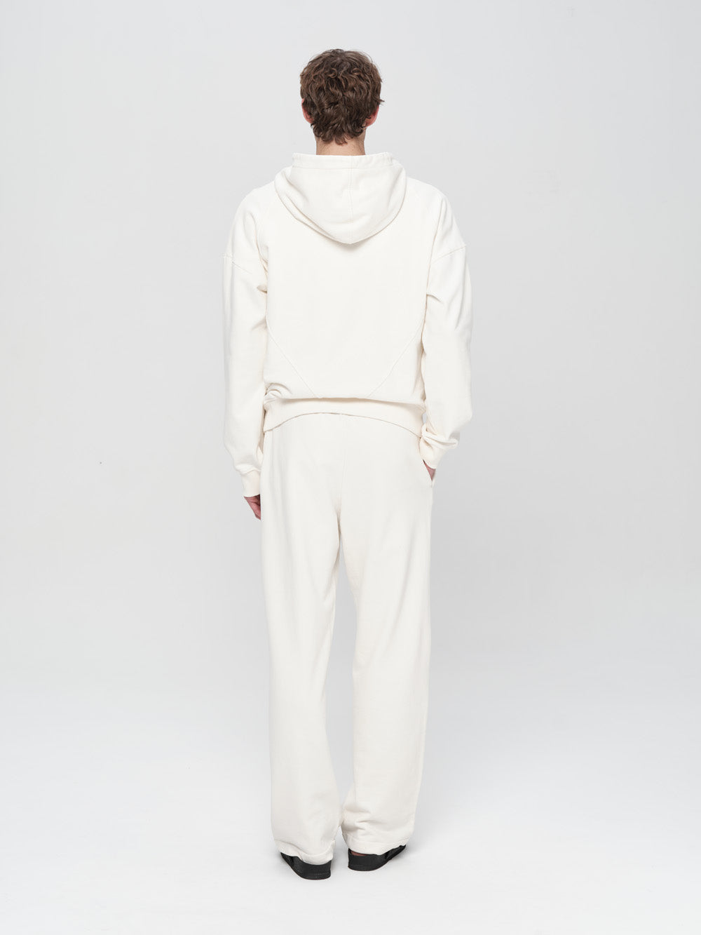 Person wearing a white hoodie and pants on a light gray background