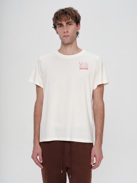 Person wearing a white t-shirt with a small graphic on a plain background