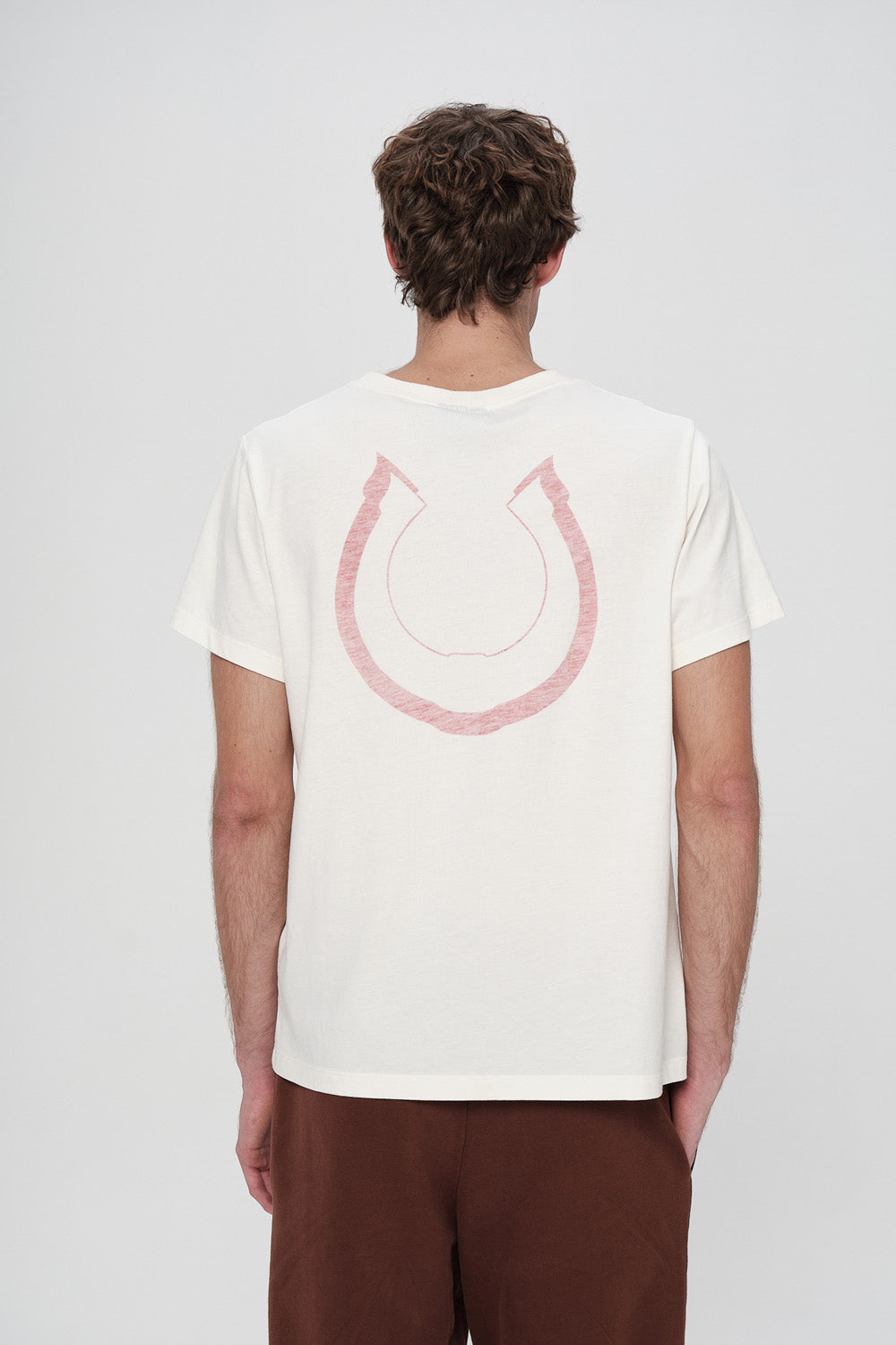 Person wearing a white t-shirt with a pink graphic design on the back against a plain background