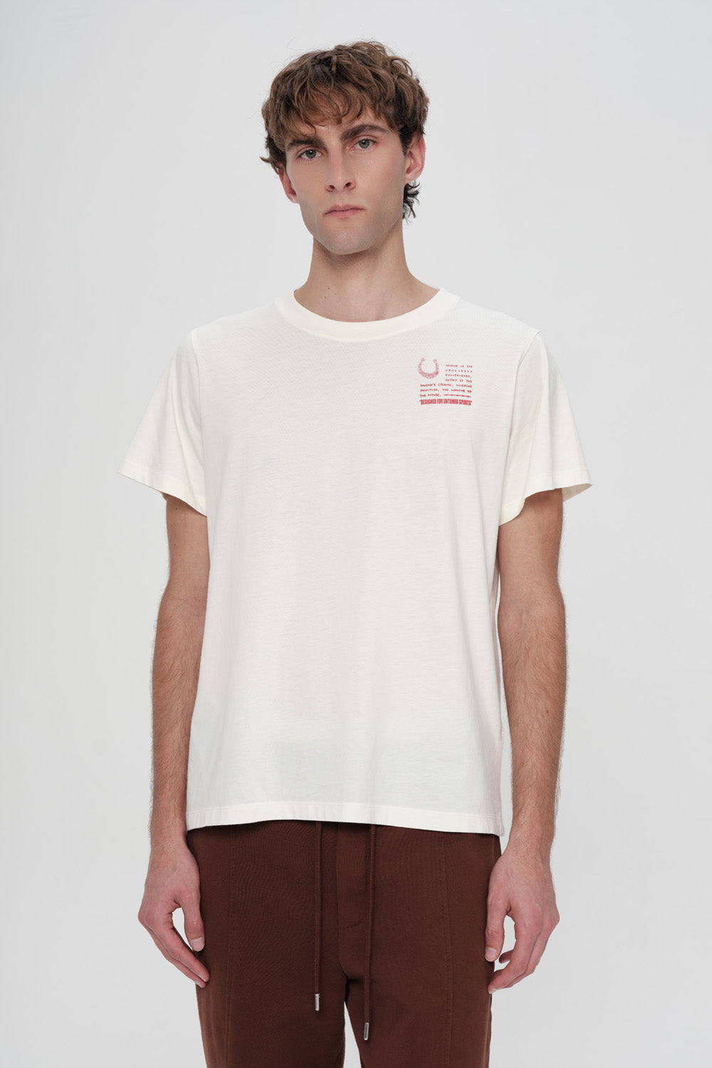 Person wearing a white t-shirt with a small red logo on a plain background