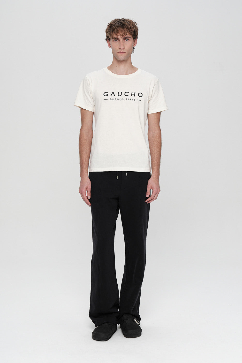 Person wearing a white t-shirt with 'Gaucho' logo and black pants on a white background