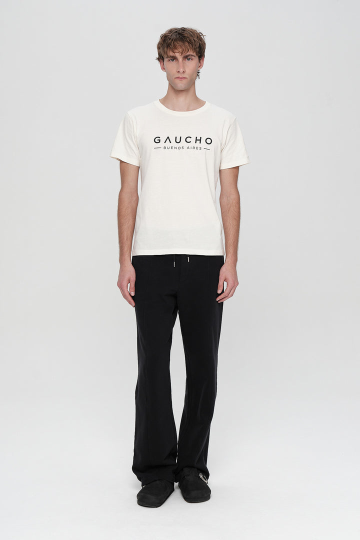 Person wearing a white t-shirt with 'Gaucho' logo and black pants on a white background