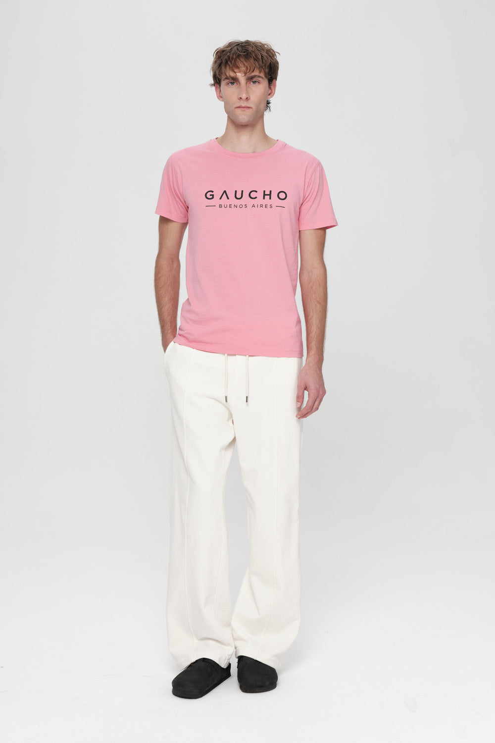 Person wearing a pink 'Gaucho' t-shirt and white pants on a white background