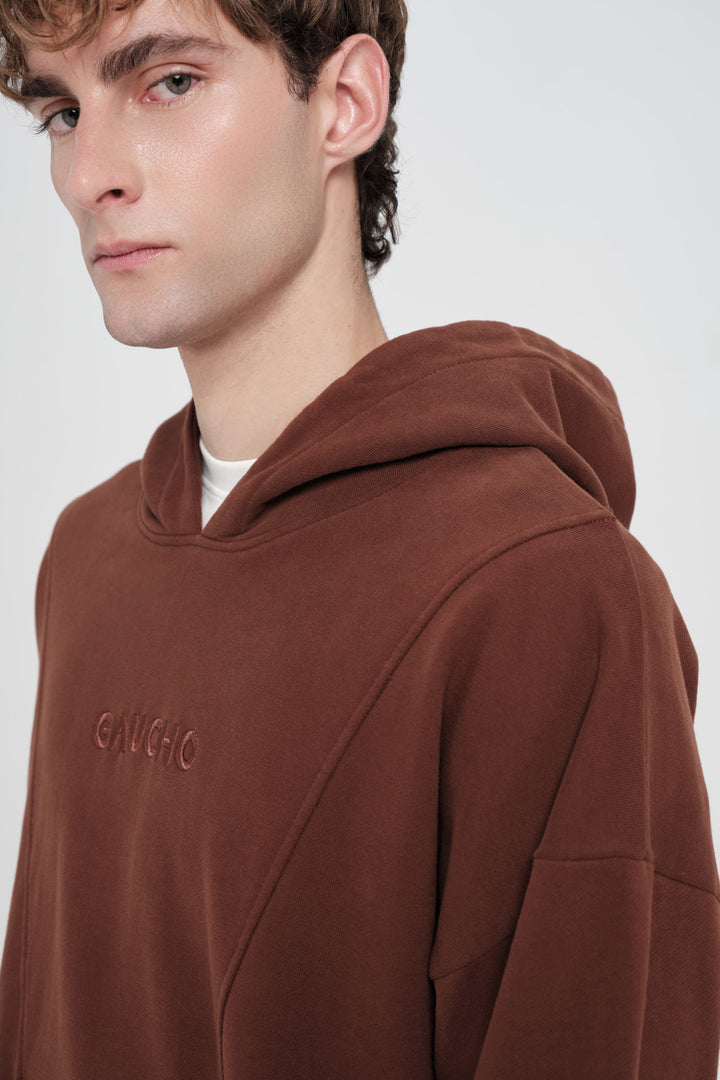 Man wearing a brown hoodie with 'Gaucho' branding on a white background