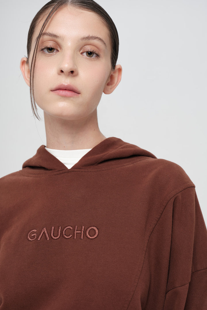 Person wearing a brown hoodie with 'GAUCHO' branding on a plain background