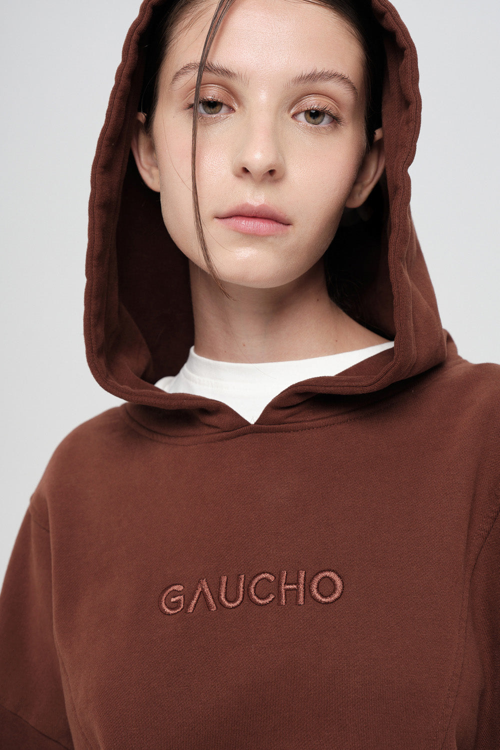 Person wearing a brown hoodie with 'GAUCHO' branding on a plain background