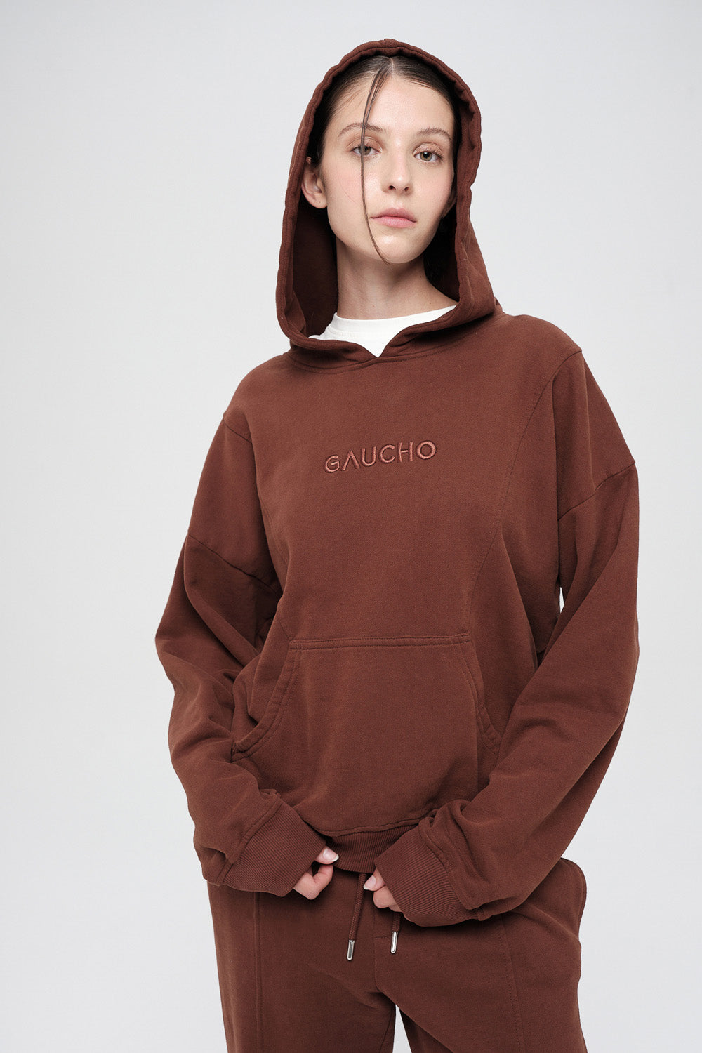Person wearing a brown hoodie with 'GAUCHO' branding on a white background
