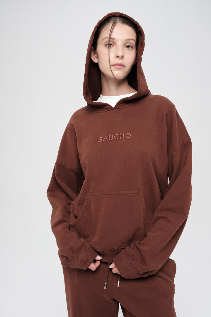 Person wearing a brown hoodie with 'GAUCHO' branding on a white background