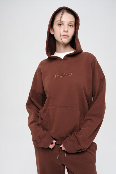 Person wearing a brown hoodie with 'GAUCHO' branding on a white background