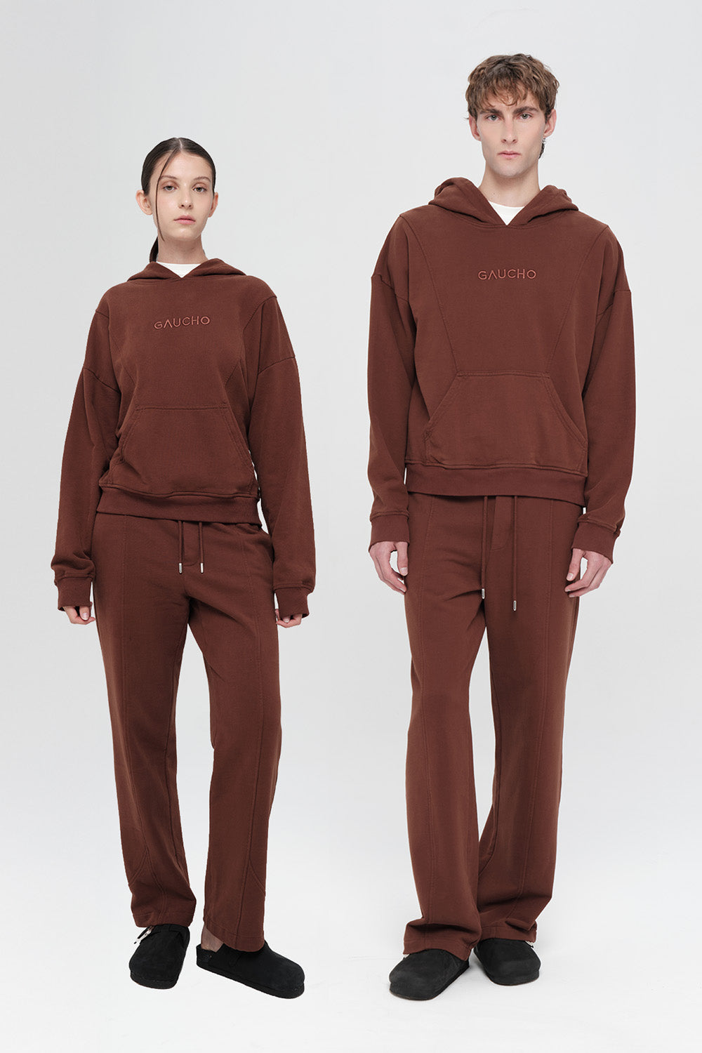 Two people wearing matching brown hoodies and pants on a white background