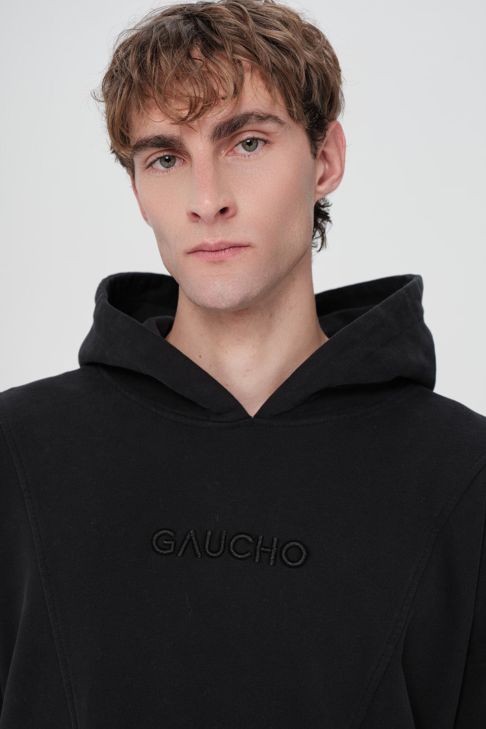 Person wearing a black hoodie with 'Gaucho' branding on a white background