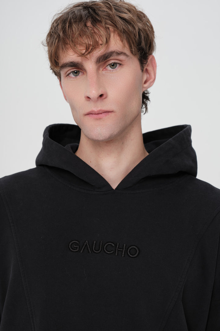 Person wearing a black hoodie with 'Gaucho' branding on a white background