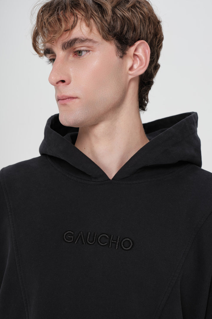Person wearing a black hoodie with 'Gaucho' branding on a plain background