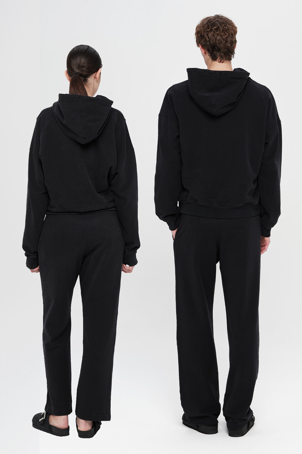 Two people wearing black hoodies and pants from different angles on a white background