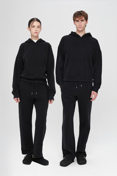 Two people wearing matching black hoodies and pants on a white background