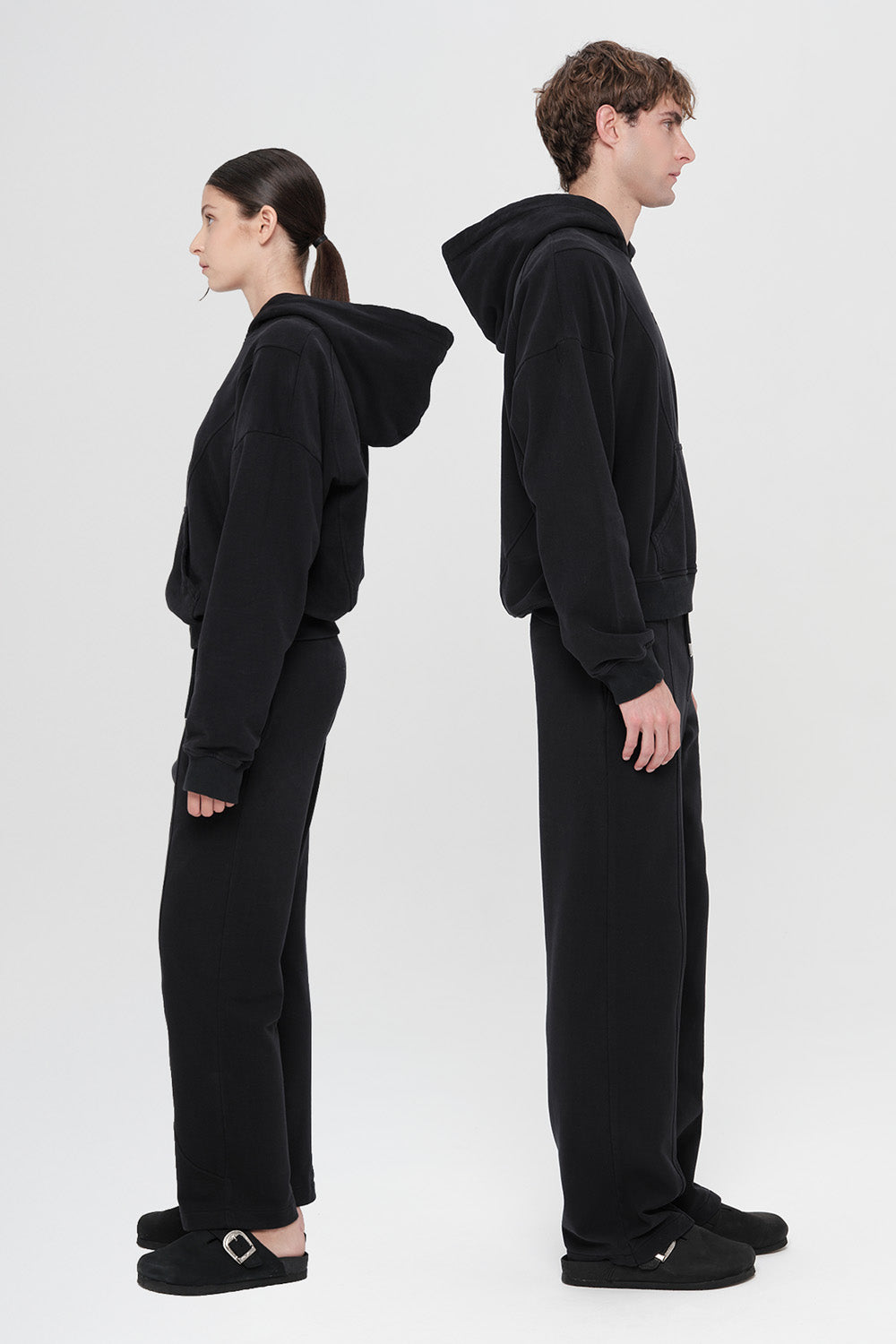 Two people wearing black hoodies and pants standing back-to-back on a white background