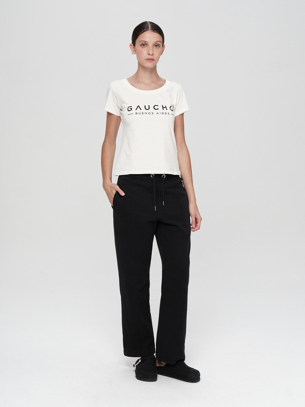 Person wearing a white t-shirt with 'Gaucho' logo and black pants on a light gray background