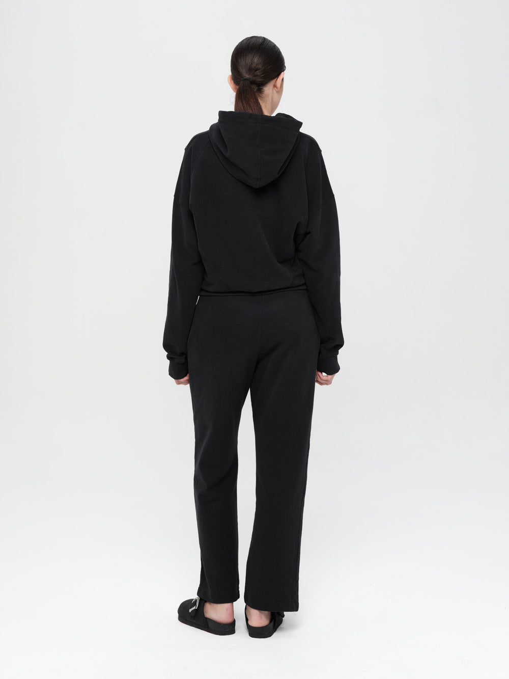 Person wearing a black hoodie and pants on a white background