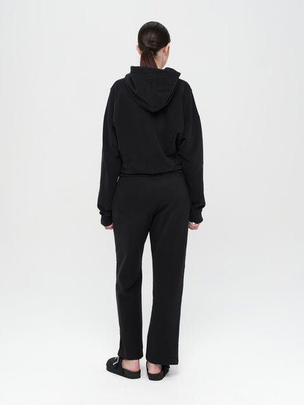 Person wearing a black hoodie and pants on a white background